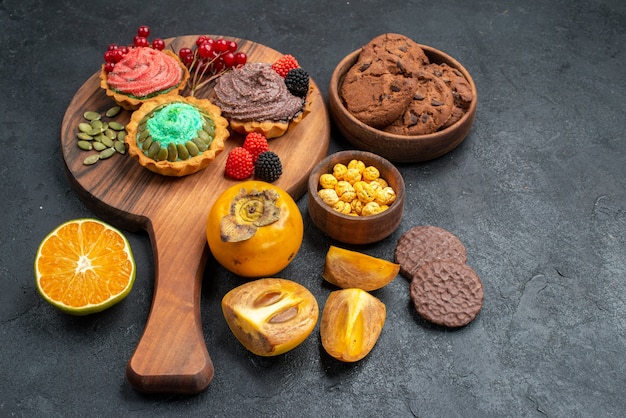 Vue de face de délicieux gâteaux avec des biscuits et des fruits sur fond sombre