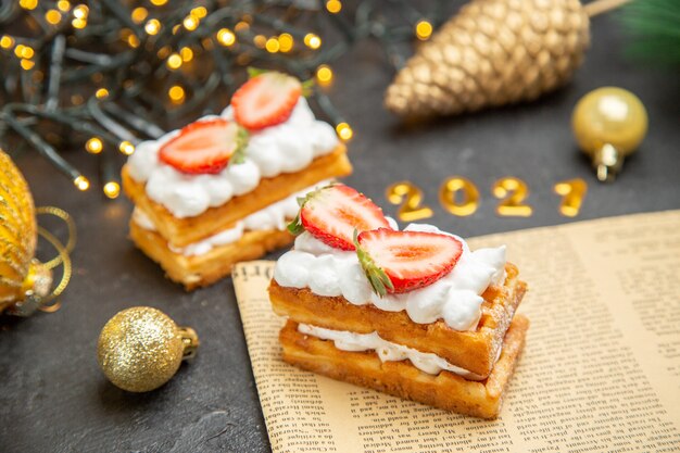 Vue de face de délicieux gâteaux à la crème avec des fraises autour des jouets d'arbre du nouvel an sur fond sombre gâteau photo douce crème dessert