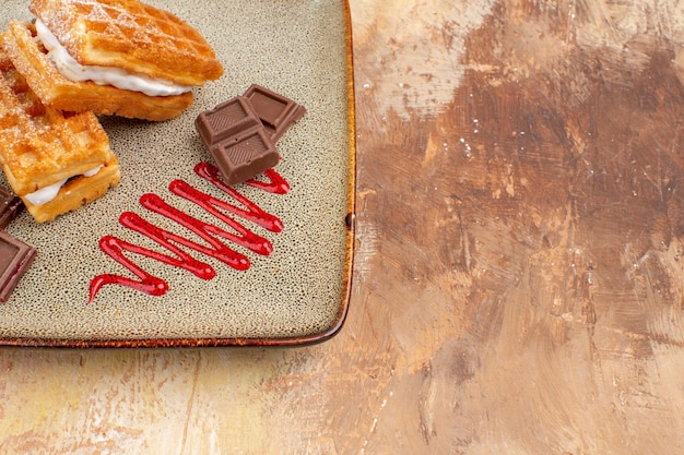 Vue de face de délicieux gâteaux à la gaufre avec des barres de chocolat sur fond marron