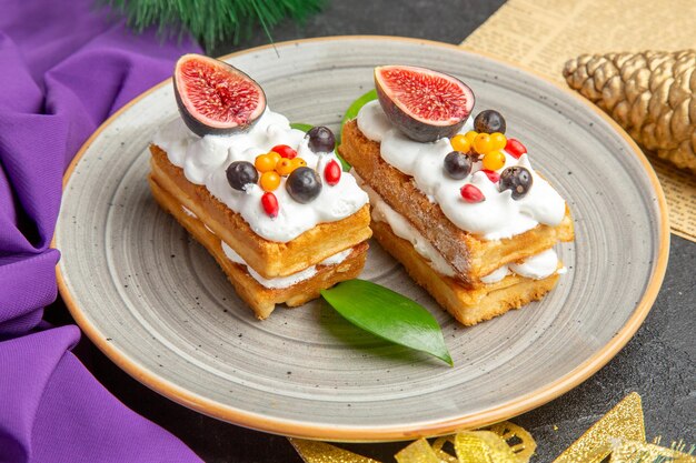 Vue de face de délicieux gâteaux de gaufres avec des fruits autour de jouets d'arbre de vacances sur fond sombre