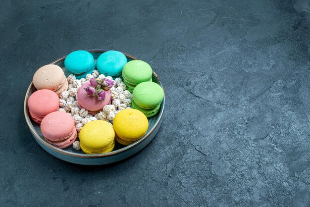 Vue de face de délicieux macarons français avec des bonbons à l'intérieur du plateau sur un espace sombre