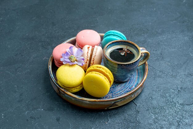 Vue de face de délicieux macarons français avec une tasse de café dans un espace sombre