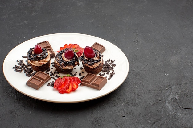 Vue de face de délicieux petits gâteaux avec des barres de chocolat et des fraises sur fond noir gâteau au chocolat et au cacao thé sucré