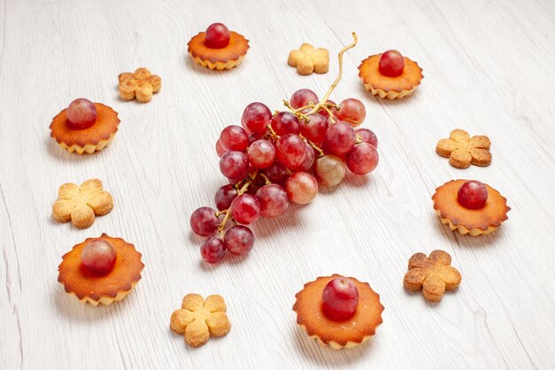 Vue de face de délicieux petits gâteaux avec des raisins et des biscuits sur fond blanc dessert thé aux fruits biscuit biscuit tarte au gâteau