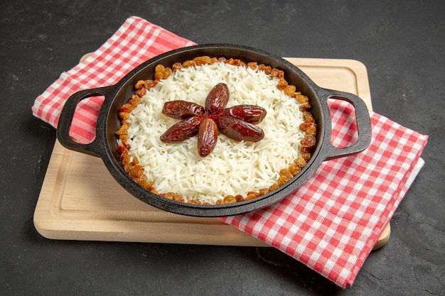 Vue de face délicieux plat de riz cuit plov avec différents raisins secs sur une surface sombre plat de raisins secs nourriture riz dîner huile