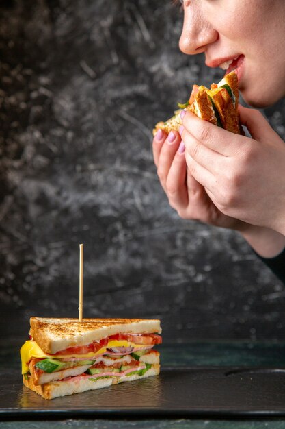 Vue de face délicieux sandwich au jambon se faire manger par une femme sur une surface sombre