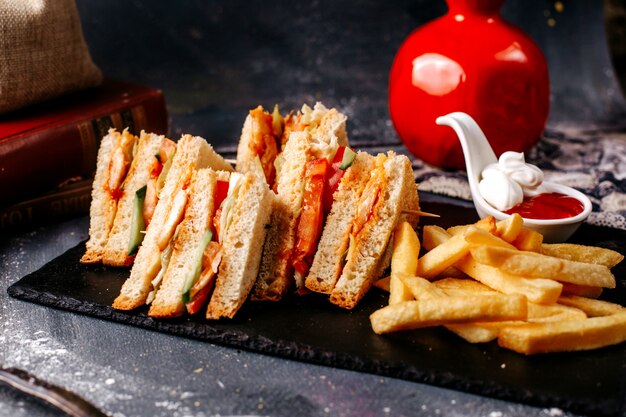 Vue de face de délicieux sandwichs tranchés avec des frites sur le bureau gris