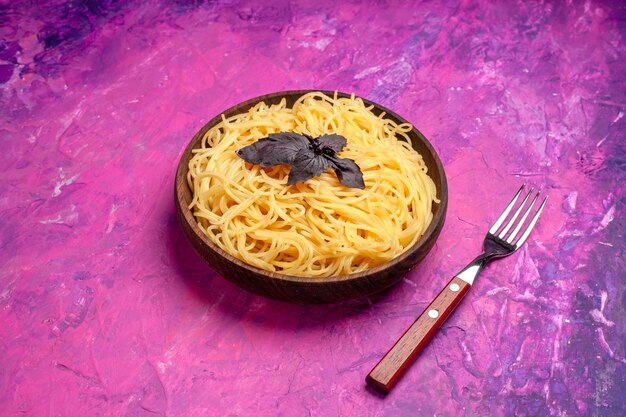 Vue de face de délicieux spaghettis cuits à l'intérieur de la plaque sur un plat de pâtes de repas de pâte de table rose