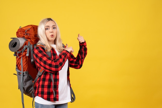 Vue de face demandé femme blonde avec son sac à dos pointant avec les doigts derrière