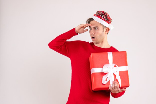 Vue de face demandé jeune homme avec bonnet de Noel debout sur blanc