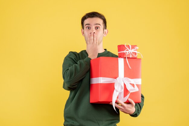 Vue de face demandé jeune homme avec cadeau de Noël debout sur jaune