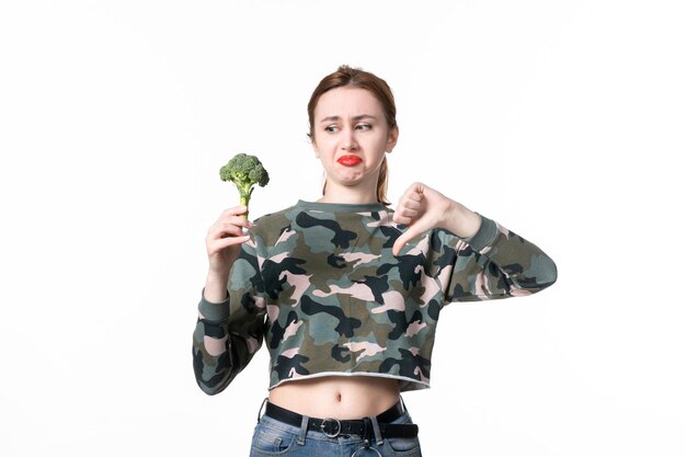 Vue de face déplu à une jeune femme tenant un petit brocoli sur blanc