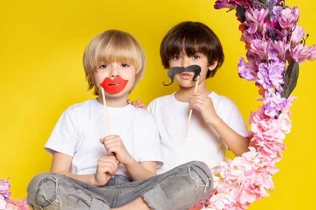 Une vue de face deux garçons adorables doux avec des moustaches assis sur la fleur fait stand sur le sol jaune