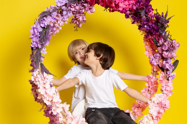 Une vue de face deux garçons assis sur le stand de fleurs en t-shirts blancs sur le bureau jaune