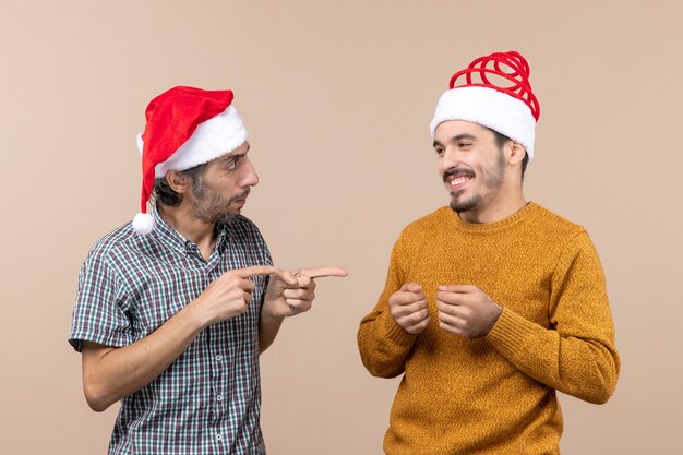 Vue de face deux gars avec des chapeaux de père Noël un doigt pointé montrant l'autre sur fond isolé beige