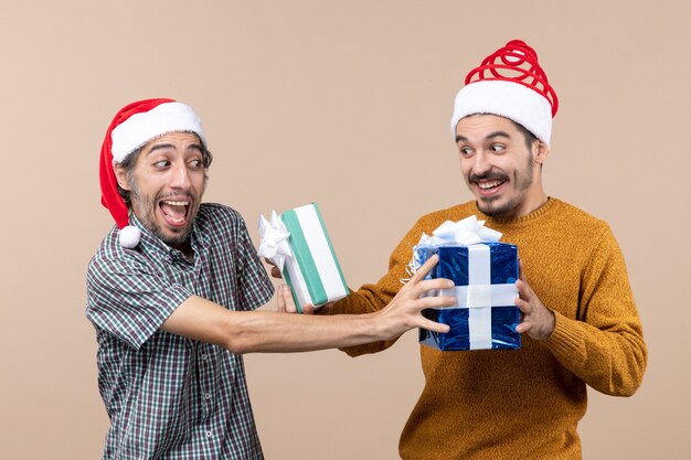 Vue de face deux gars confus échangeant leurs cadeaux de Noël sur fond isolé beige