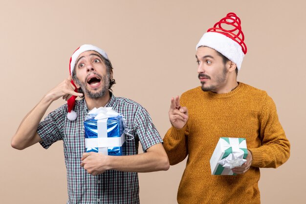 Photo gratuite vue de face deux gars l'un montrant appelez-moi signe de téléphone l'autre signe de victoire et tenant des cadeaux