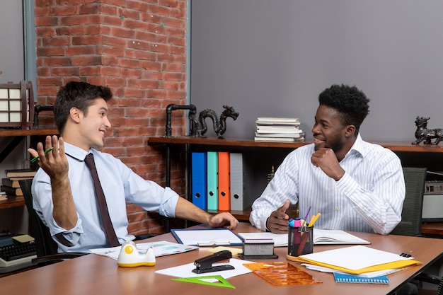 Vue de face deux hommes d'affaires satisfaits assis au bureau travaillant ensemble