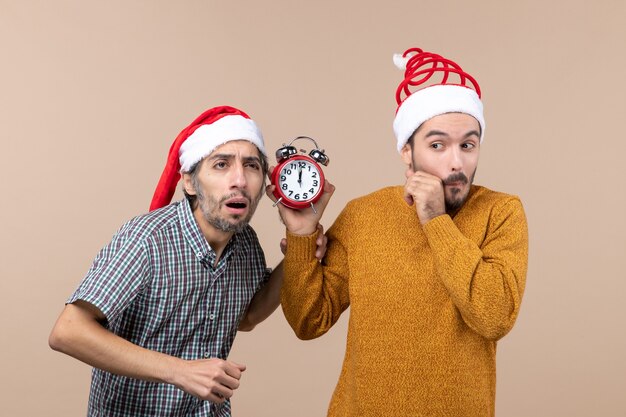 Vue de face deux hommes confus l'un écoutant et l'autre tenant un réveil sur fond isolé beige