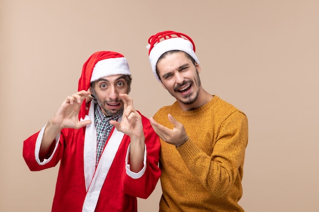 Vue de face deux hommes l'un faisant signe de la caméra et l'autre le pointant sur fond isolé beige