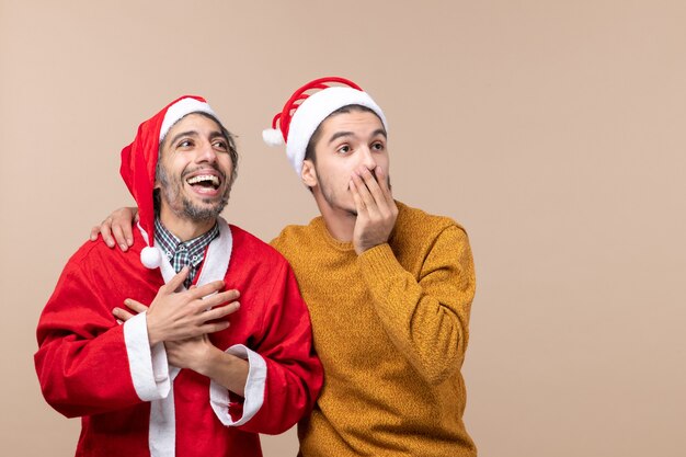 Vue de face deux hommes heureux à la fois en regardant quelque part sur fond isolé beige