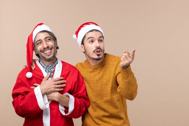 Vue de face deux hommes heureux à la fois regardant quelque part les yeux sur fond isolé beige