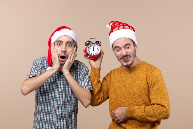 Vue de face deux hommes de Noël un choquant et l'autre tenant un réveil sur fond isolé beige