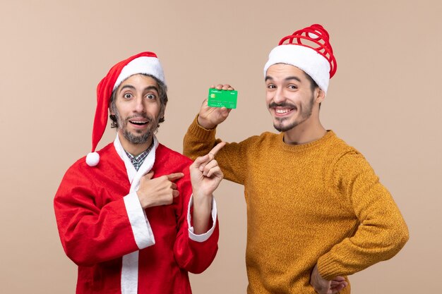 Vue de face deux hommes de Noël un avec manteau de père Noël et l'autre avec crédit mettant sa main sur une taille sur fond isolé beige