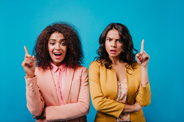 Vue de face de deux jeunes femmes exprimant des émotions sur le mur bleu