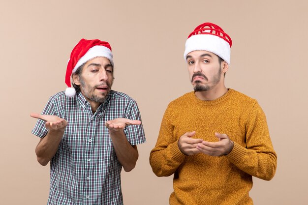 Vue de face deux mecs avec des chapeaux de père Noël déroutant sur fond isolé beige
