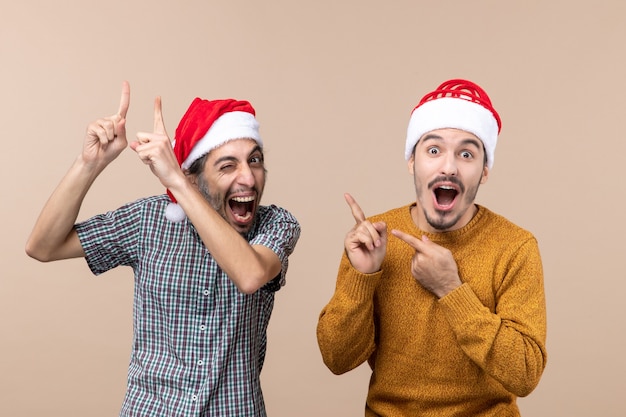 Vue de face deux mecs ravis avec des chapeaux de père Noël l'un montrant quelque chose à l'autre sur fond isolé beige