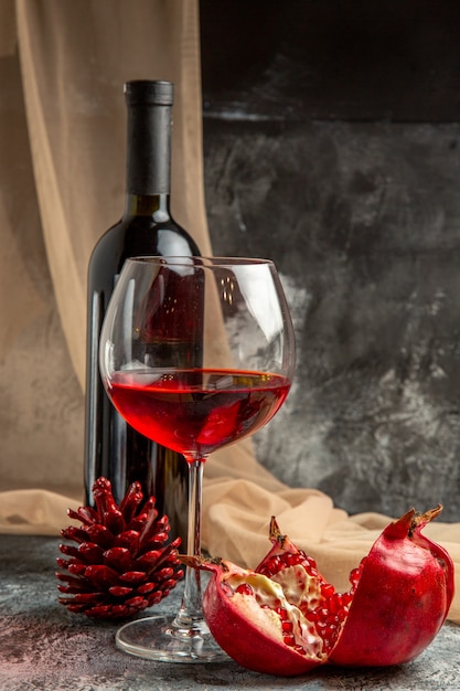 Vue de face de deux verres et d'une bouteille avec un délicieux vin rouge sec et un cône de conifère de grenade ouvert sur fond de glace