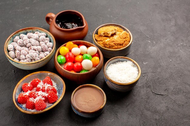 Vue de face différents bonbons colorés avec confitures sur fond sombre biscuit au thé aux bonbons