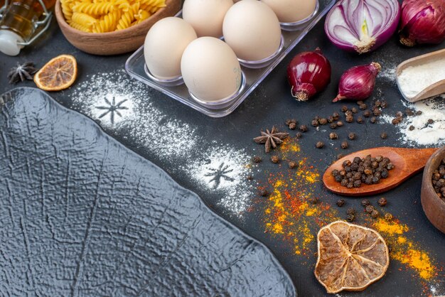 Vue de face différents ingrédients oeufs farine pâtes crues et assaisonnements sur fond sombre couleur végétale lait pâte sombre oeuf d'oiseau