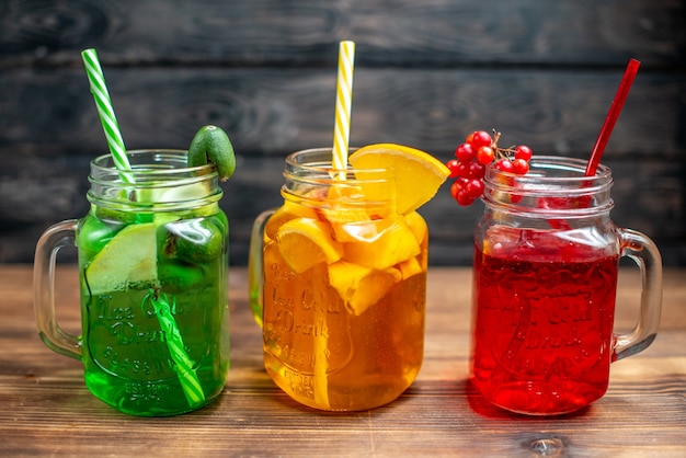 Photo gratuite vue de face différents jus de fruits frais à l'intérieur de canettes sur le bureau en bois marron