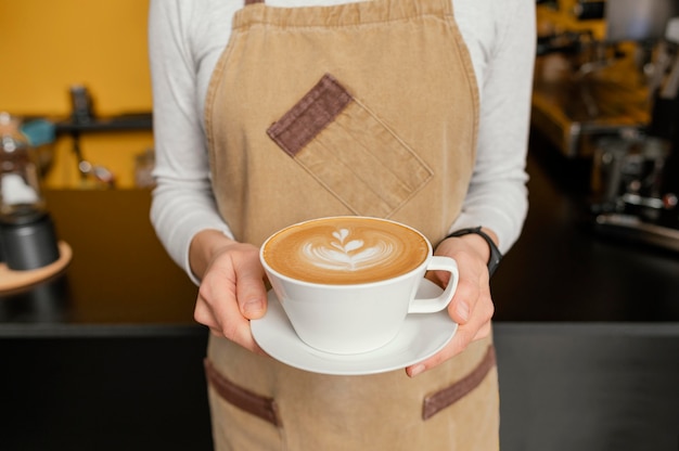 Vue de face du barista féminin tenant une tasse de café décorée dans les mains