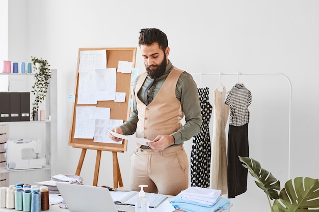 Photo gratuite vue de face du beau créateur de mode masculin travaillant en atelier avec des papiers