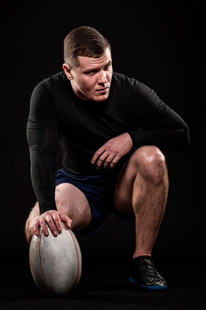 Vue de face du beau joueur de rugby athlétique tenant le ballon