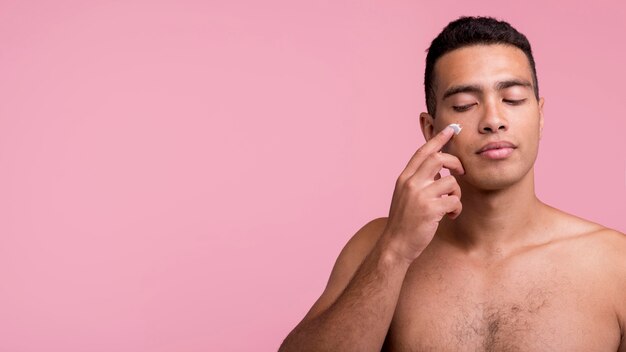 Vue de face du bel homme, appliquer la crème pour le visage avec copie espace