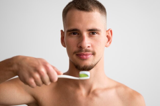 Vue de face du bel homme tenant une brosse à dents avec du dentifrice dessus