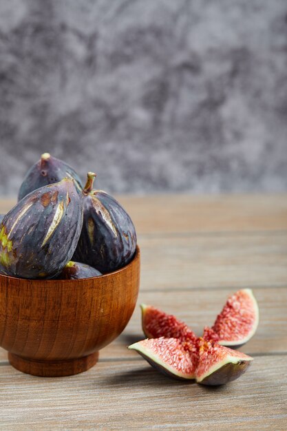 Vue de face du bol de figues noires et tranches de figues sur table en bois.