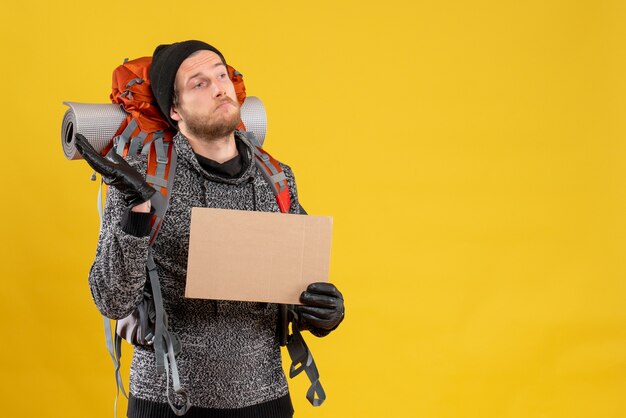 Vue de face du campeur homme confus avec des gants en cuir et sac à dos tenant un carton vierge