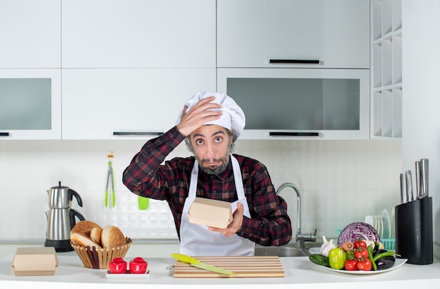 Vue de face du chef masculin demandé brandissant une boîte à hamburger dans la cuisine