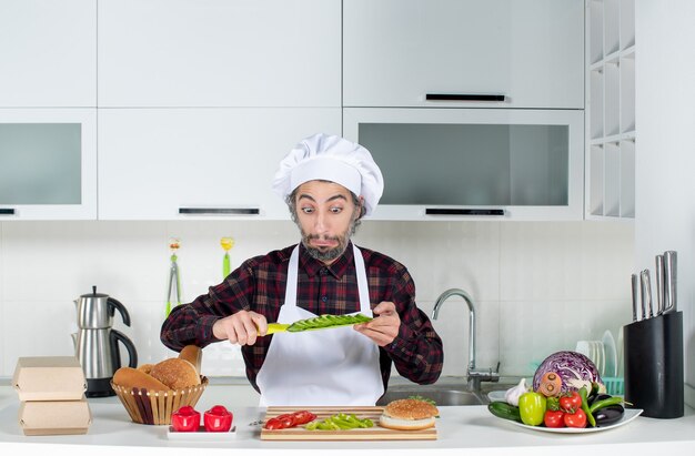 Vue de face du chef masculin demandé brandissant un couteau coupant des légumes dans la cuisine