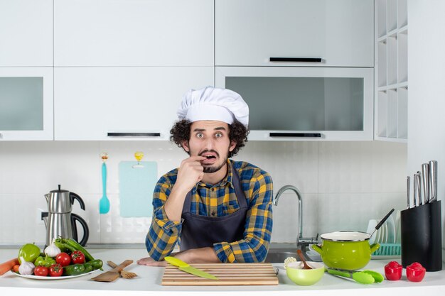 Vue de face du chef masculin avec des légumes frais se sentant confus dans la cuisine blanche
