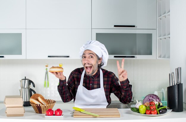 Vue de face du chef masculin tenant du pain faisant le signe de la victoire dans la cuisine