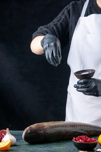 Vue de face du chef en tablier blanc saupoudré de sel sur des graines de grenade de poisson frais dans un bol d'ail sur une table