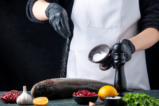 Vue de face du chef en tablier saupoudré de sel sur des graines de grenade de poisson frais dans un bol sur une table