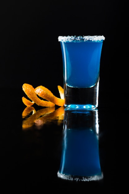 Vue de face du cocktail bleu en verre à shot avec zeste d'orange et bord de sel