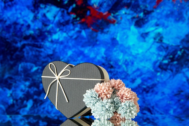 Vue de face du coffret coeur avec couvercle noir et fleurs colorées sur fond abstrait bleu